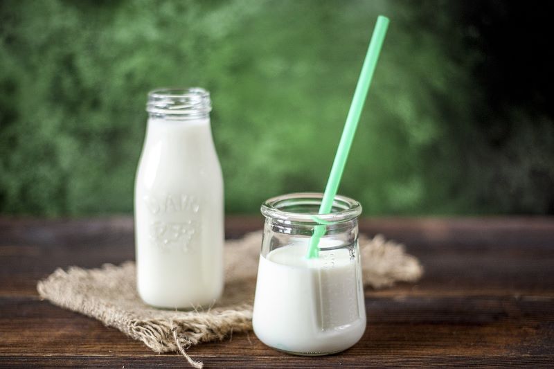 Ein Glas Milch mit Strohhalm und eine Glasflasche gefüllt mit Milch auf einem Holztisch