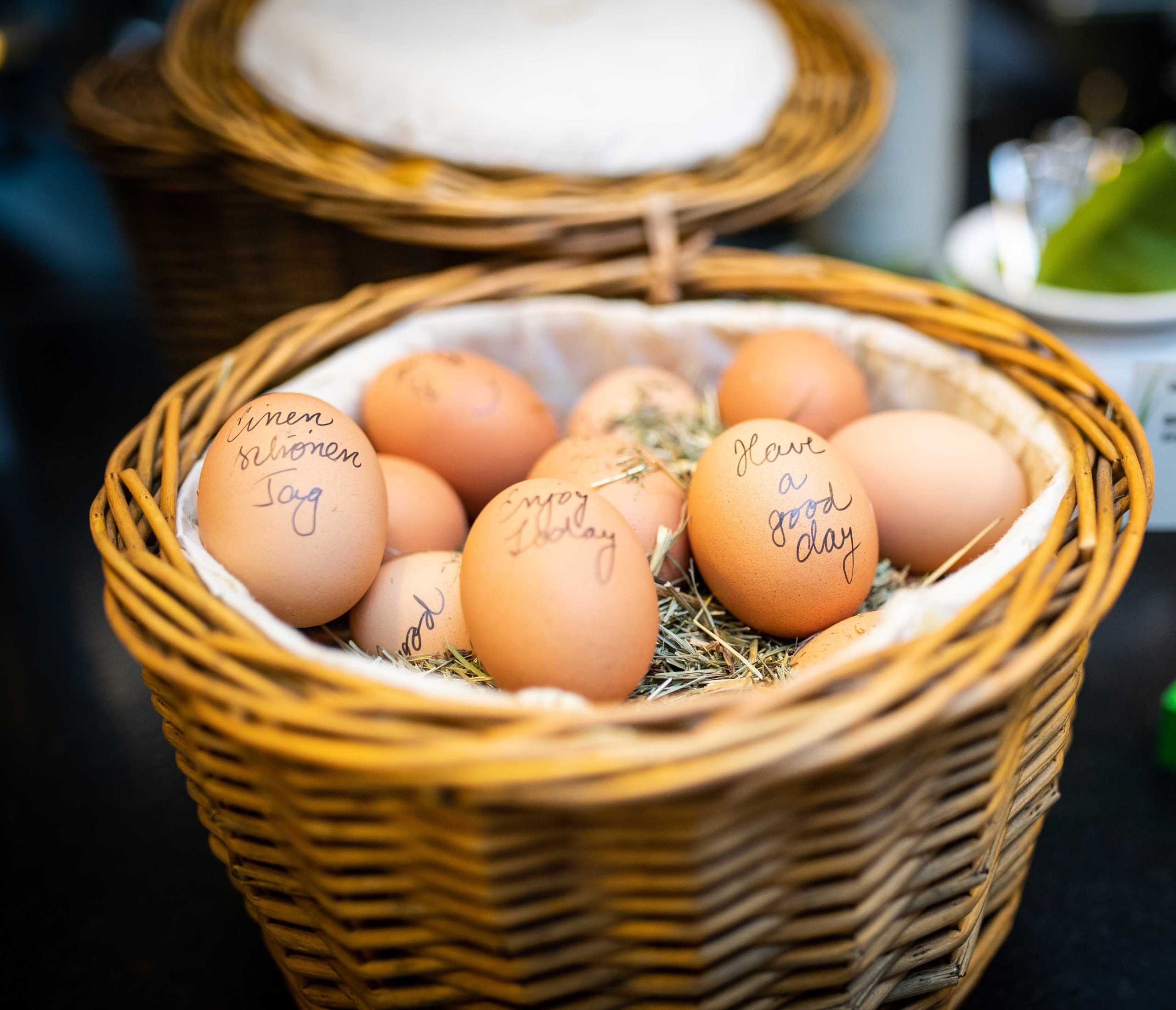 Gekochte Eier liegen in einem Korb auf Heu und sind mit Wünschen für einen guten Tag beschriftet