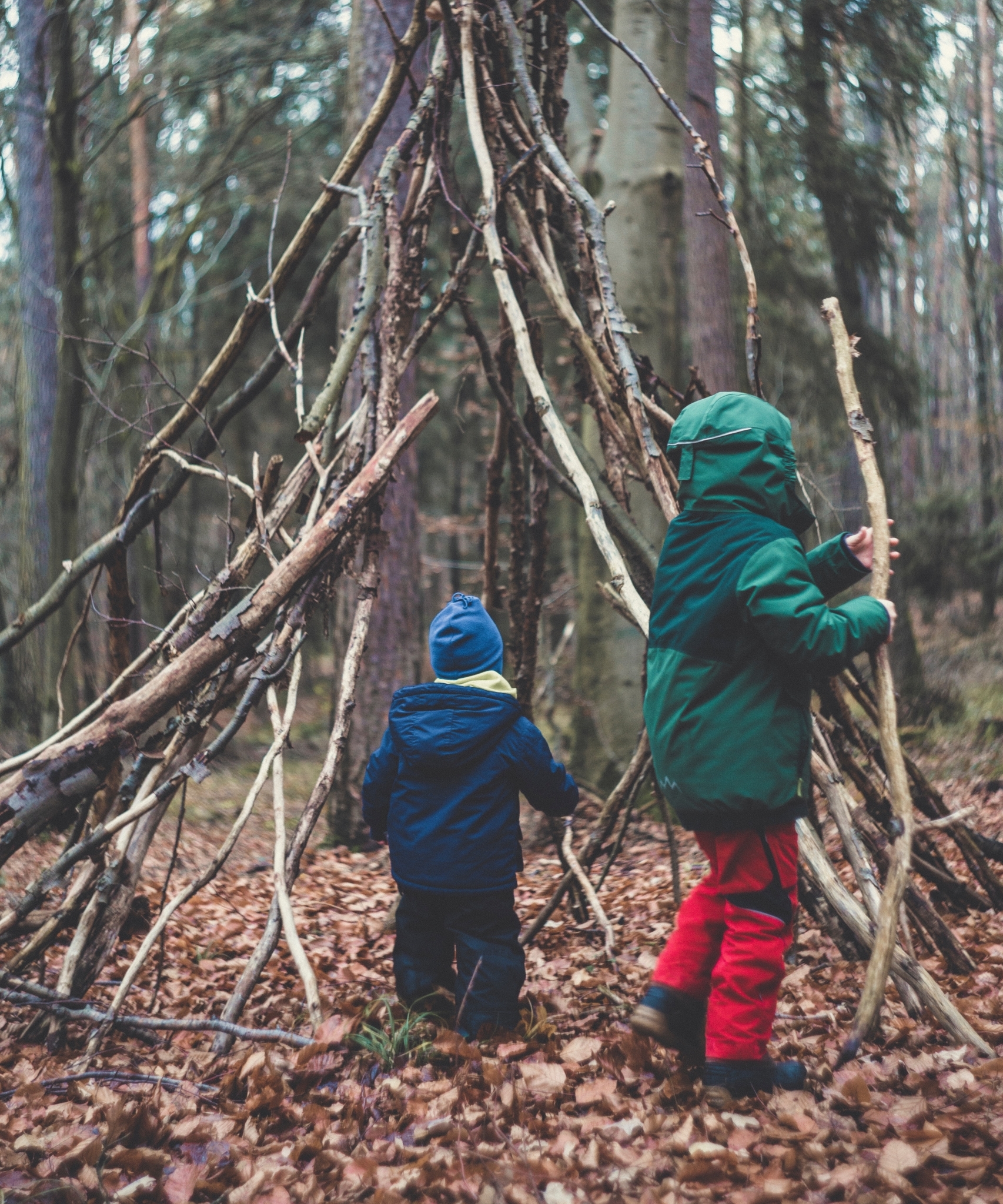 Zwei Kinder spielen im Wald und bauen ein Tipi mit großen Stöcken