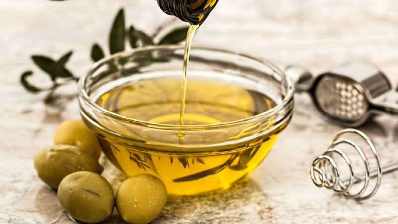 Olivenöl in einer kleinen Glasschale, davor liegen ein paar Oliven