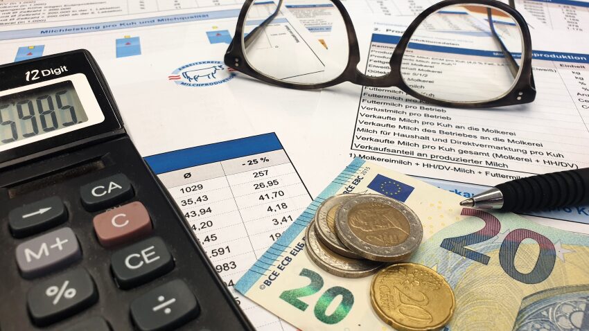 Taschenrechner, Geld, Brille, Unterlagen und ein Stift liegt auf einen Tisch