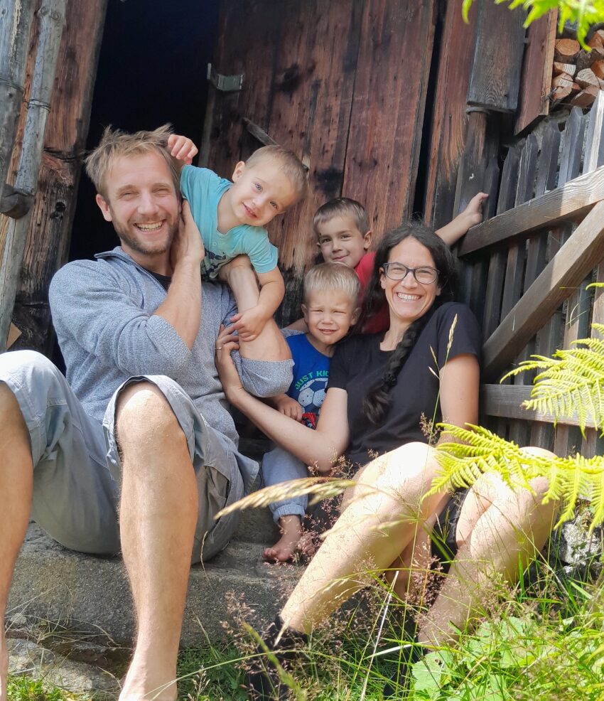 Eine Familie mit drei Kindern sitzt vor einem Schuppen