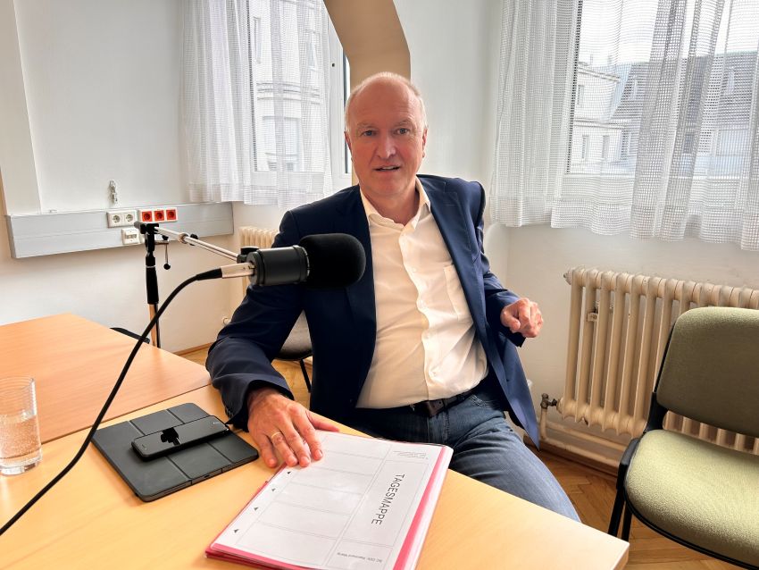 Portrait von SC DDr. Reinhard Mang, der am Interviewtisch sitzt, mit Mikrofon und die Mappe vor ihm liegend