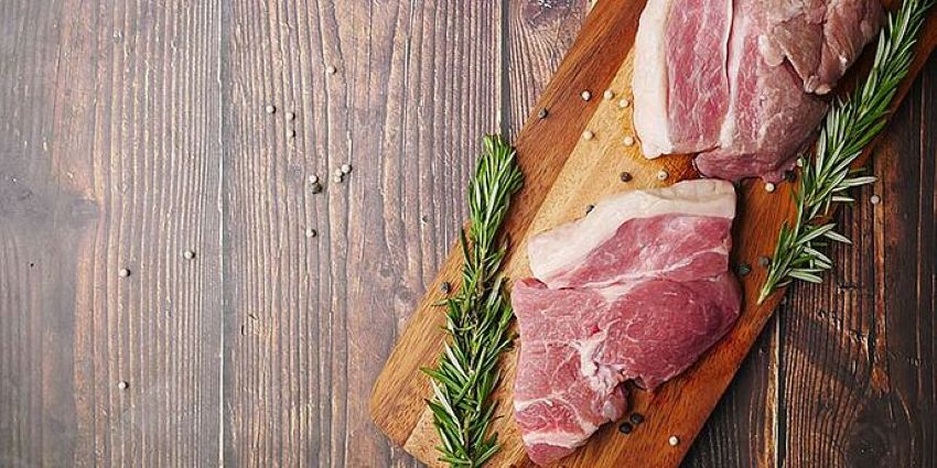Fleischteile vom Schwein auf einem Holzbrett schön angerichtet mit Rosmarin