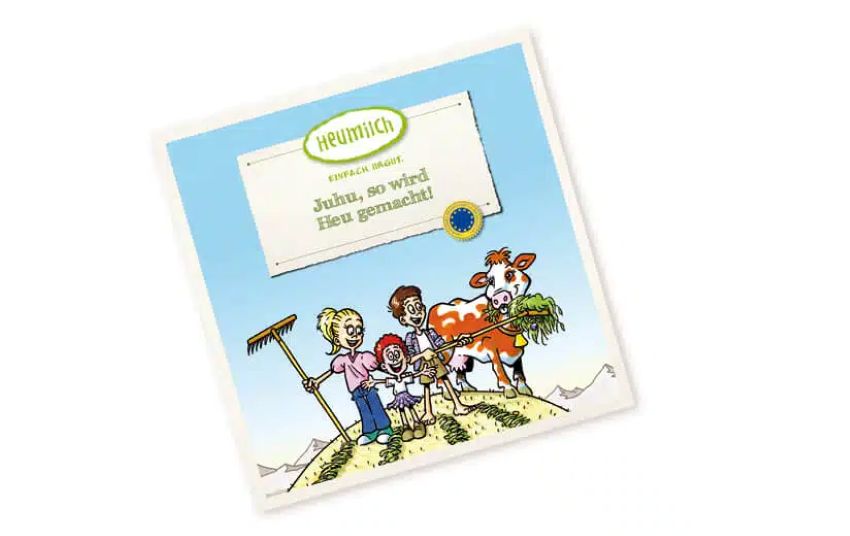 Drei Kinder auf der Wiese, zwei davon halten einen Rechen in der Hand, daneben steht eine Kuh, die Gras frisst