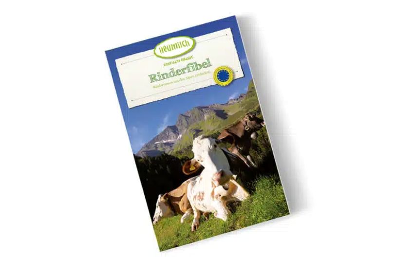 zwei Rinder liegen auf der Weide, eines steht, im Hintergrund sieht man Berge