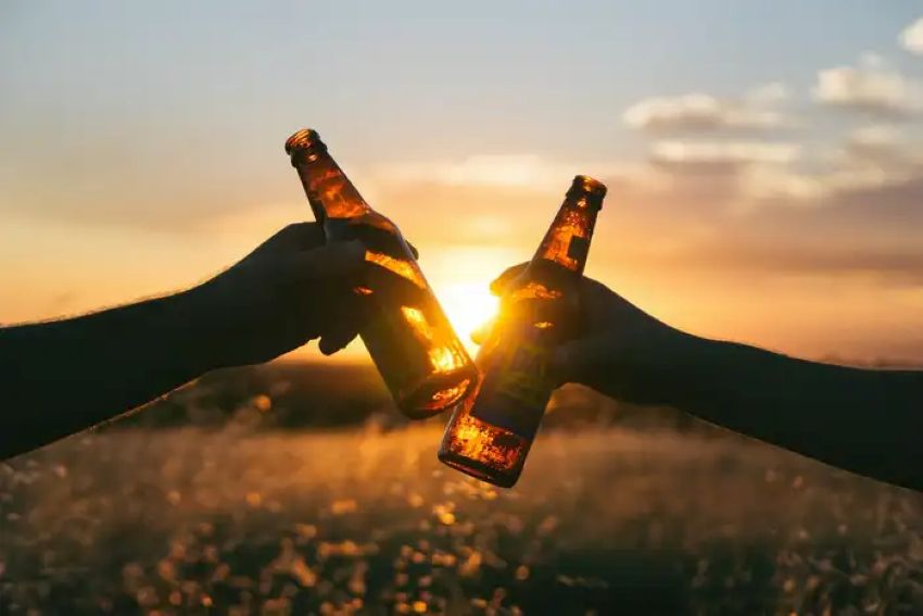 Zwei Personen die mit Bierflaschen bei Sonnenuntergang anstoßen