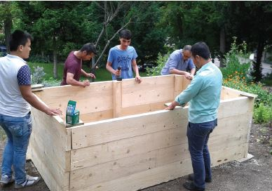 Eine Gruppe von Menschen die gemeinsam ein Hochbeet aus Holz bauen