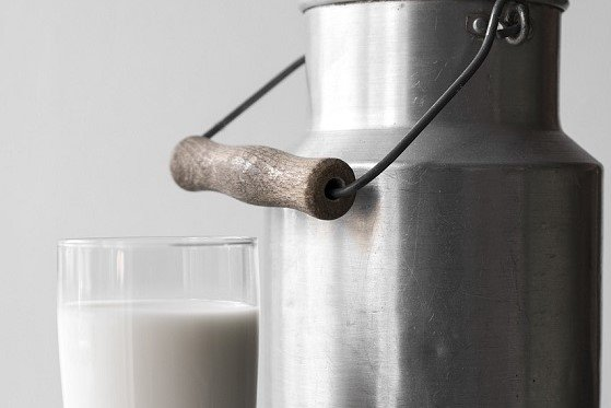 Ein Glas mit Milch und eine Milchkanne